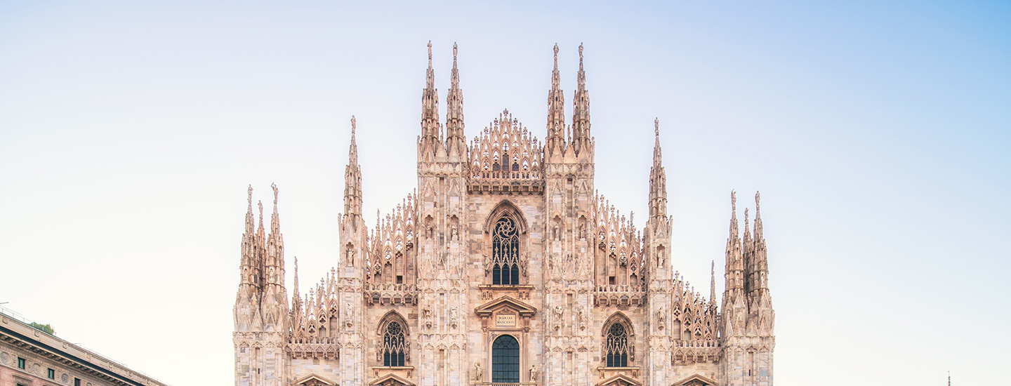 Front view of Milan Cathedral with intricate Gothic spires and carvings under a clear blue sky.