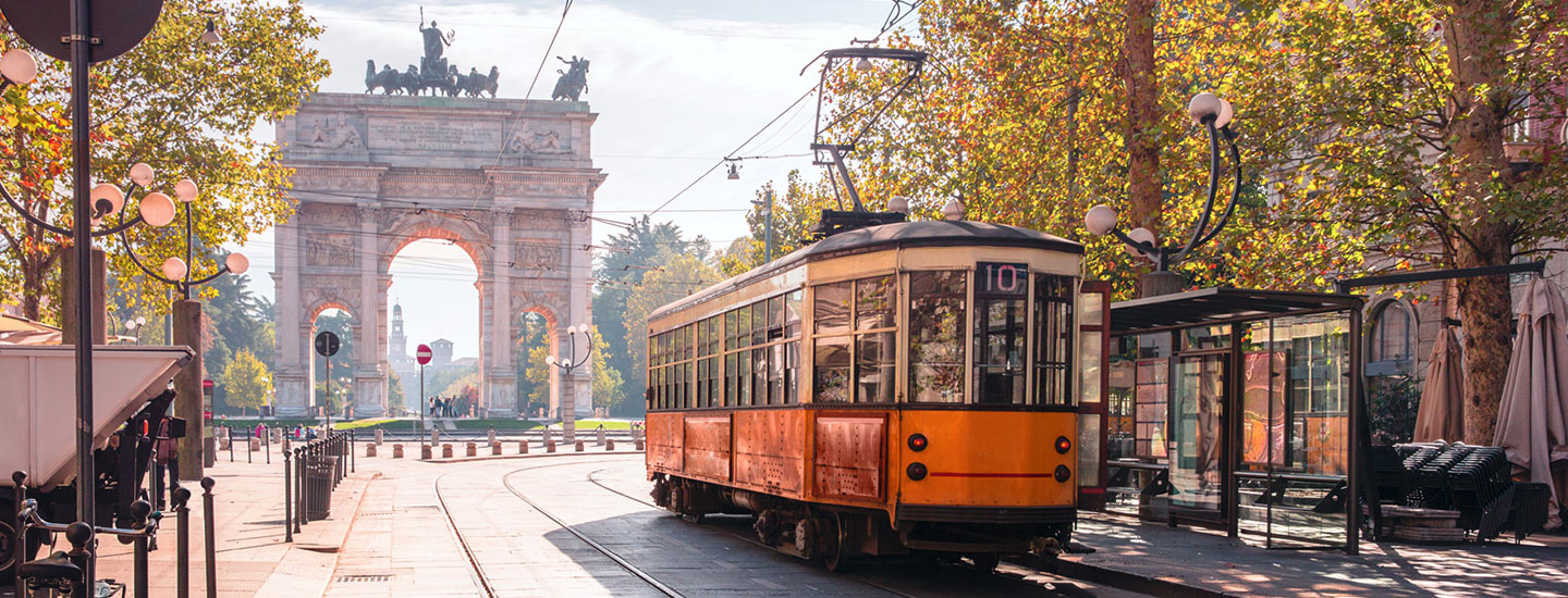 Vintage orange tram passing the Arco della Pace in Milan, surrounded by autumn trees and street lamps.
