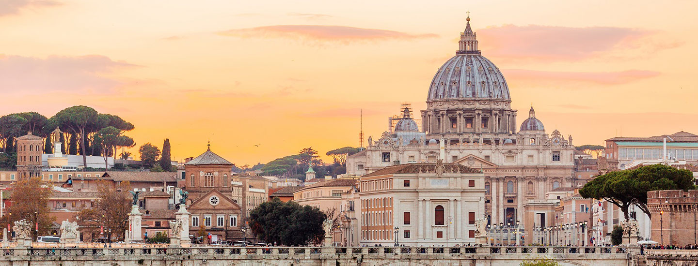 View of St. Peter's Basilica from Rome, showcasing its iconic dome rising above surrounding buildings at sunset, symbolizing the city's spiritual and architectural heritage.