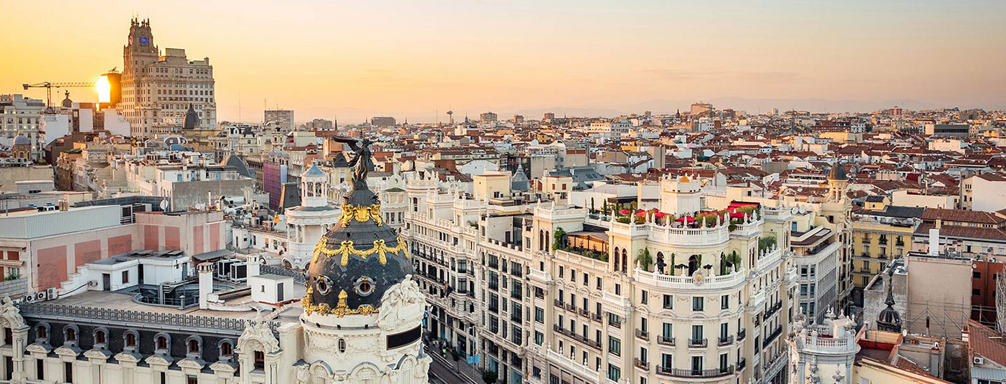 Metropolis Building in Madrid at sunset with city rooftops and warm sky.