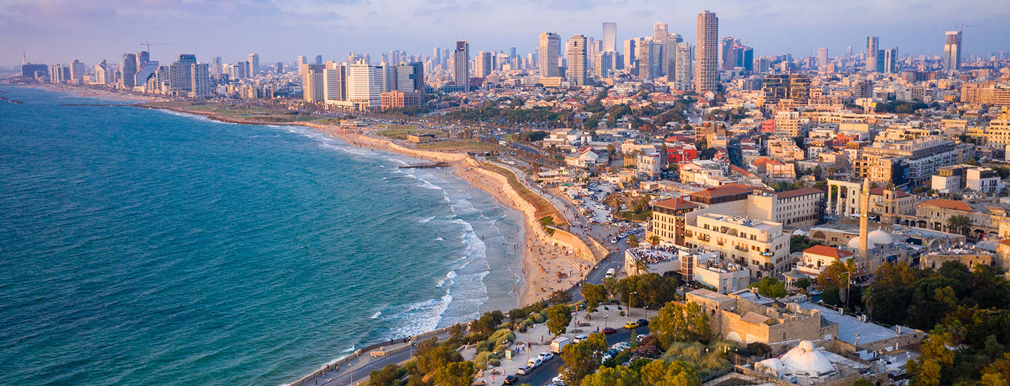 Aerial view of Tel Aviv, Israel, showing the Mediterranean coastline, busy beach, high-rise skyline, and urban greenery.