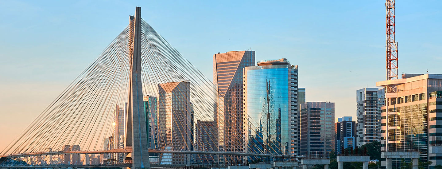 Cityscape in São Paulo, Brazil, featuring a cable-stayed bridge, modern high-rise buildings, and a tall communication tower under a clear sky.