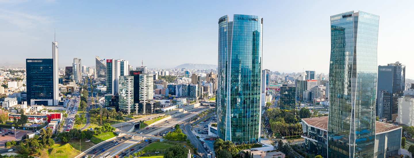 Panoramic cityscape with curved glass skyscrapers, greenery, and a clear blue sky.