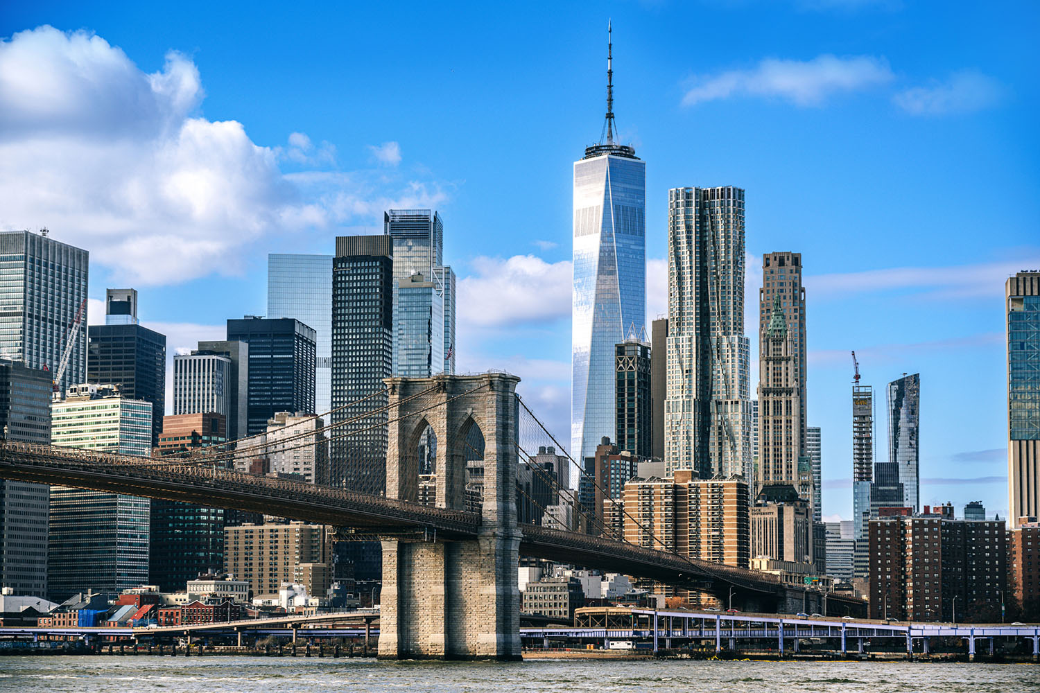 Brooklyn Bridge with Lower Manhattan skyline and clear sky in the background.