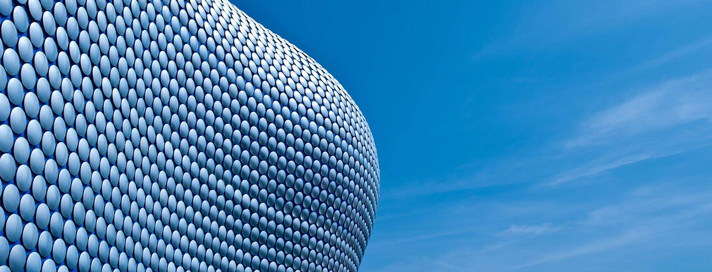 Exterior view of the Selfridges Building in Birmingham, UK, featuring a curved facade covered with circular aluminum discs under a clear blue sky.
