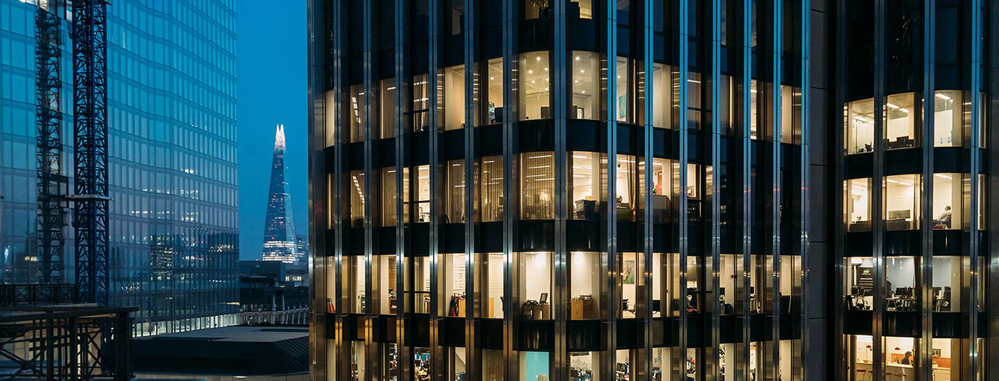 Night time view of the London skyline with illuminated office buildings and The Shard visible in the background.