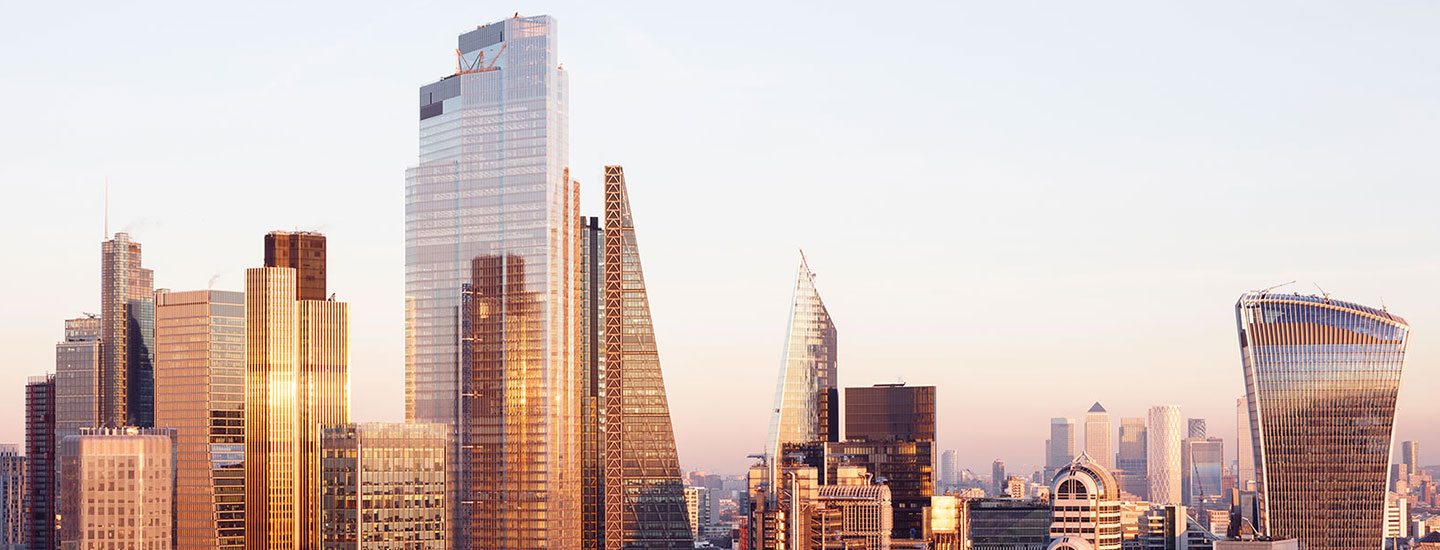 Cityscape of London, England, featuring modern skyscrapers with glass facades under warm sunrise or sunset lighting and a clear sky.