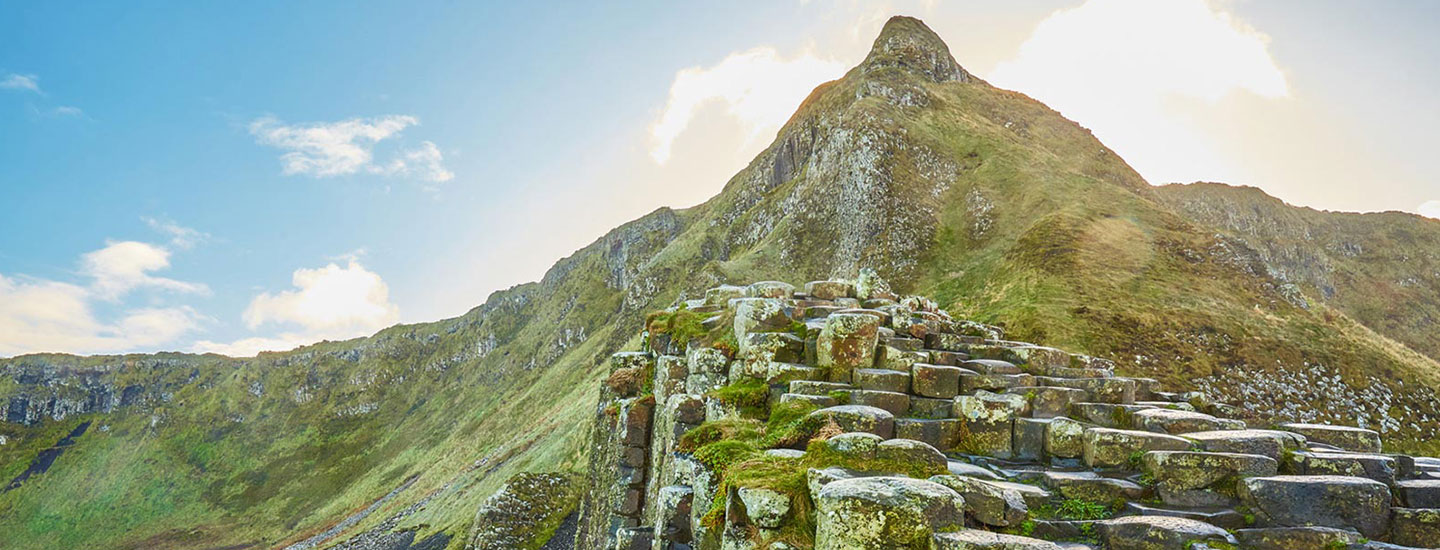 Basalt columns at Giant’s Causeway in Northern Ireland with grassy hill and blue sky.