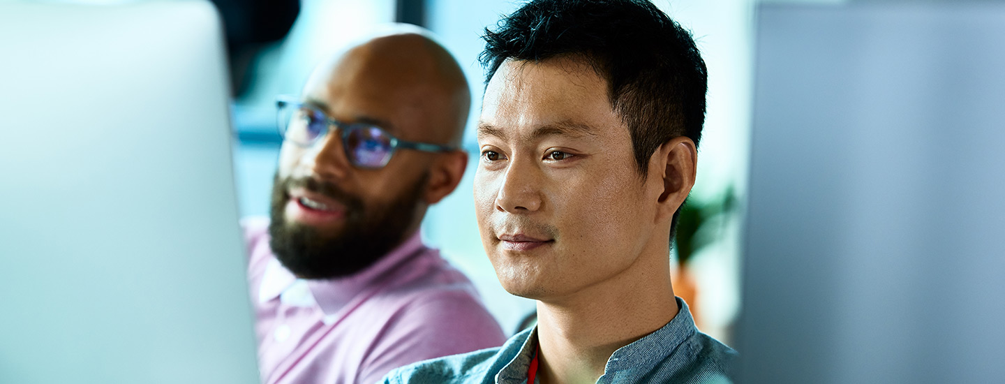 Two individuals seated in front of computer screens with blurred faces.