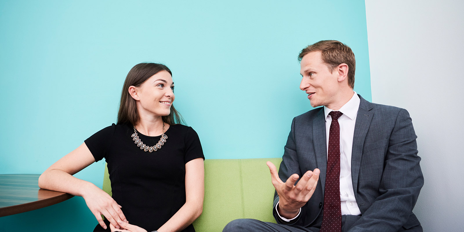 Two people sitting on a green couch against a blue wall, engaged in conversation