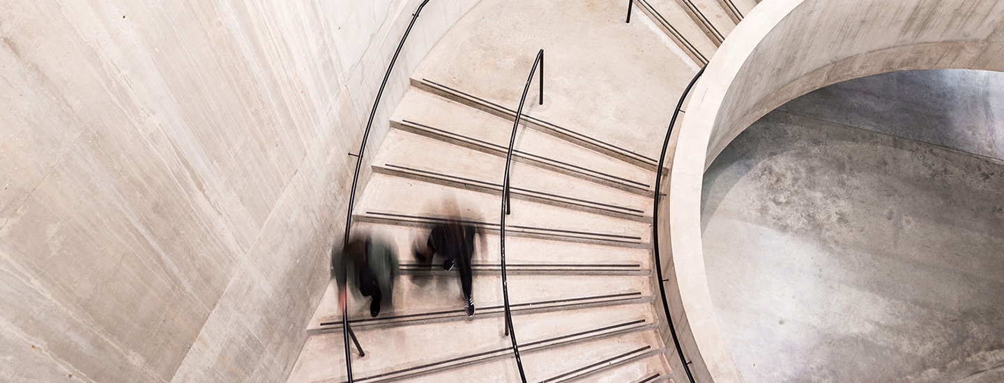 Top-down view of a modern concrete spiral staircase with metal railings and people walking on it