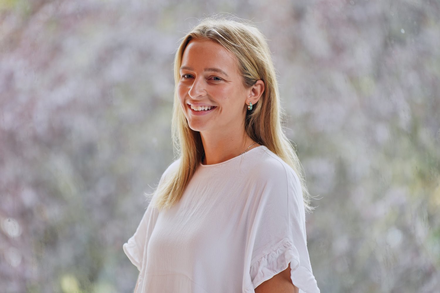 Karrie Mead, with long blonde hair and a white blouse, is pictured against a softly blurred outdoor background.